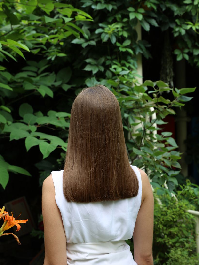 Hairdressing art: Haircut line for straight natural long hair. A woman standing backward against green climbing plant leaves